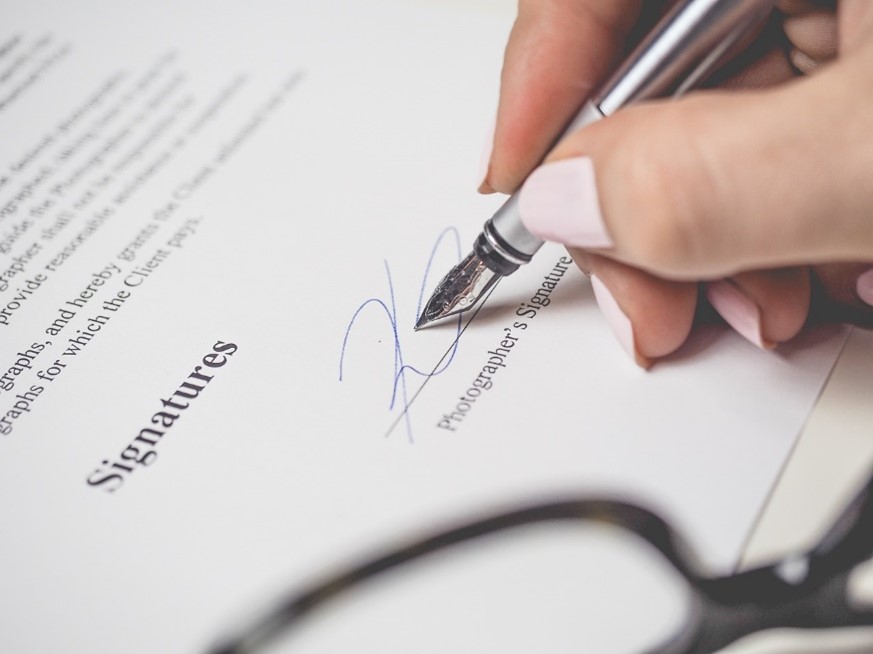 A woman’s hand signing a document with a wet signature